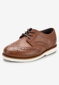 Brązowe skórzane buty z detalami brogue, zaokrąglonym noskiem i białą gumową podeszwą. Posiadają sznurowadła i gładką teksturę.
