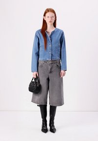 Τζάκετ με κοπή σε στυλ cropped από τζιν σε ανοιχτό μπλε, γκρίζες παντελόνες σε φαρδιά γραμμή, μαύρη τσάντα και μαύρες μπότες με ψηλή γάμπα και μεταλλικές λεπτομέρειες.