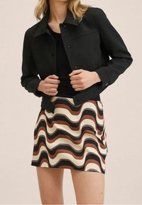 Veste noire à fermeture boutonnée et manches longues, associée à une mini-jupe à motifs ondulés en crème, marron et noir. Texture lisse.