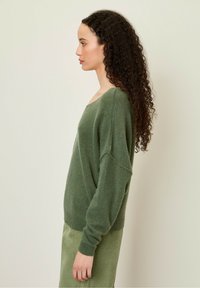 Grøn strikket sweater med løs pasform og bred halsudskæring, kombineret med en ribbet olivengrøn nederdel. Blød tekstur og afslappet silhuet.