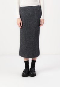Strikket grå midikjole med ribbestruktur, tettsittende liv, og avsmalnet kant. Kombinert med svarte loafers og sokker, noe som gir et strømlinjeformet utseende.