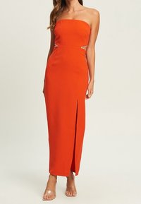 Oranges trägerloses Maxikleid mit einer figurbetonten Silhouette, seitlichen Ausschnitten und einem schulterhohen Schlitz. Glattes Material mit einem leichten Glanz.