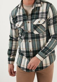 Grün-weiß kariertes Flanellhemd mit durchgehendem Knopfverschluss, zwei Brusttaschen und weicher Textur. Leichtgewichtig mit lockerem Schnitt.