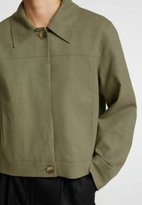Chaqueta verde oliva en tejido ligero, con cuello extendido, cierre de un solo botón y bolsillos laterales. Diseño limpio y estructurado.