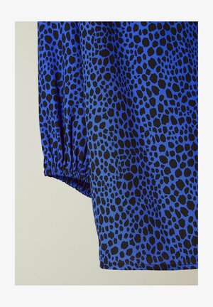 Tessuto blu con un motivo a macchie nere, con polsini delle maniche arricciati. La trama appare liscia e leggera.