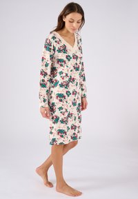 Vestaglia floreale color crema con maniche lunghe, scollatura a V, caratterizzata da un bordo in pizzo e un motivo di fiori rossi e verdi. Tessuto morbido e leggero.