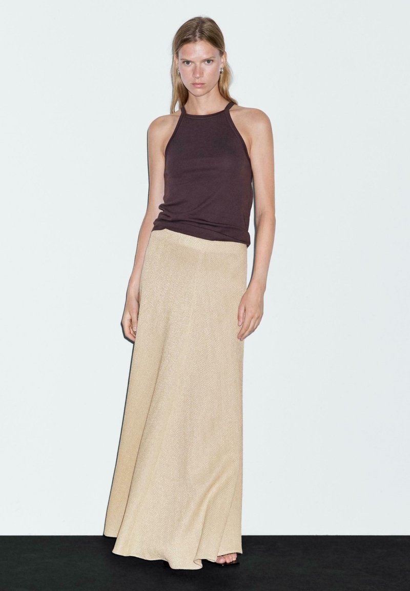 Top a fascia marrone scuro abbinato a una lunga gonna beige con un motivo a spina di pesce, che mette in mostra una texture liscia e una silhouette fluttuante.