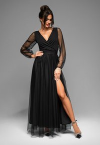 Abito maxi nero con maniche lunghe trasparenti e scollatura profonda a V. Presenta un corpetto aderente, una gonna fluida e uno spacco alto sulla coscia.