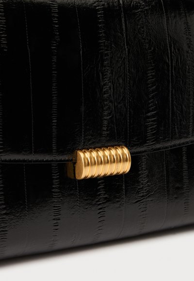 Gros plan d'une surface en cuir noir texturé avec des crêtes verticales et un fermoir horizontal doré strié.