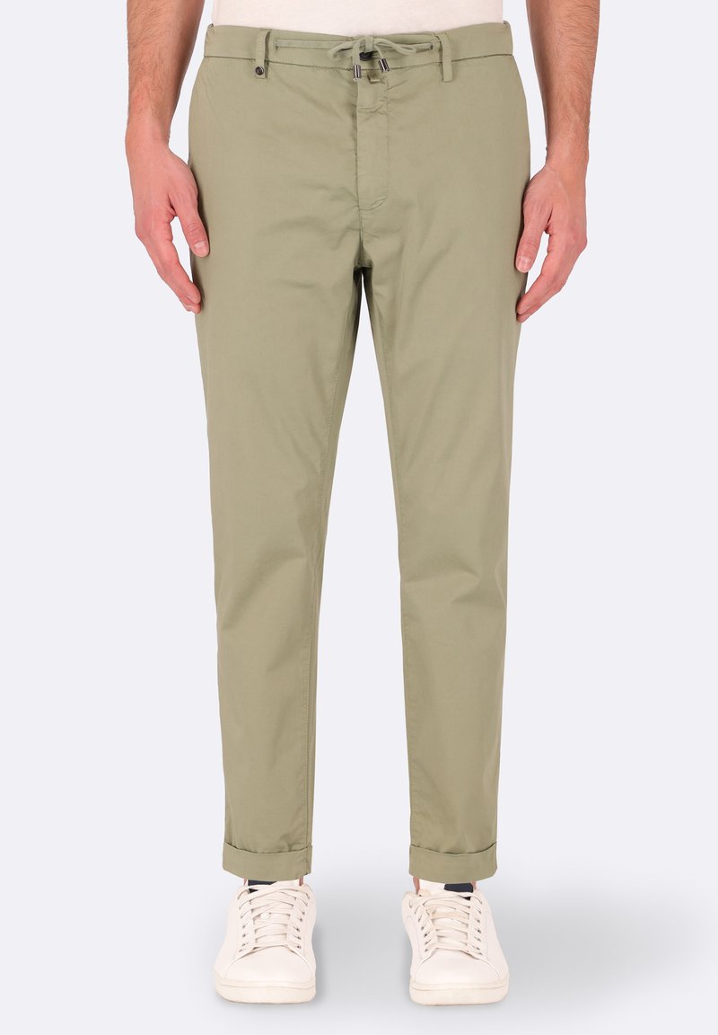 Chinos verde oliva chiaro con una texture liscia, fitting slim, tasche anteriori e orli arrotolati, abbinati a sneaker bianche.