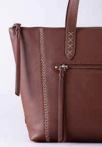 Brown leather tote bag featuring braided accents, vertical stitching in contrasting color, and a zippered pocket on the front.
