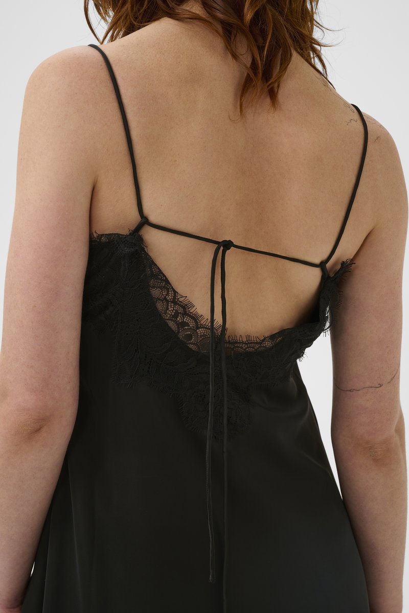 Robe noire en satin avec un dos décolleté orné de détails en dentelle, fines bretelles ajustables et un lien noué au dos. Texture lisse.