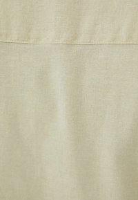 Lichtbeige, gestructureerde stof met een subtiele weving, een glad oppervlak en een horizontale naad nabij het midden. Geen zichtbare patronen of accenten.