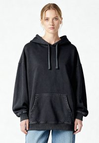 Sweat à capuche en coton noir avec une grande poche frontale, capuche ajustable avec cordon et poignets et ourlet côtelés, présentant une coupe décontractée et ample.