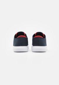 Marineblaue Mesh-Sneaker mit roten Akzenten, weißer Sohle, runder Form und gepolstertem Kragen. Sie verfügen über eine glatte Textur und ein minimalistisches Design.