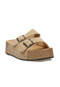 Sandalia de ante beige, tipo deslizable, con dos correas ajustables, hebillas plateadas, plataforma tipo corcho y suela de goma negra con detalles de tachuelas.