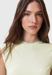 Top senza maniche di colore verde chiaro realizzato in un tessuto morbido ed elasticizzato; presenta un colletto alto. Una collana in argento a catena intrecciata valorizza il collo.