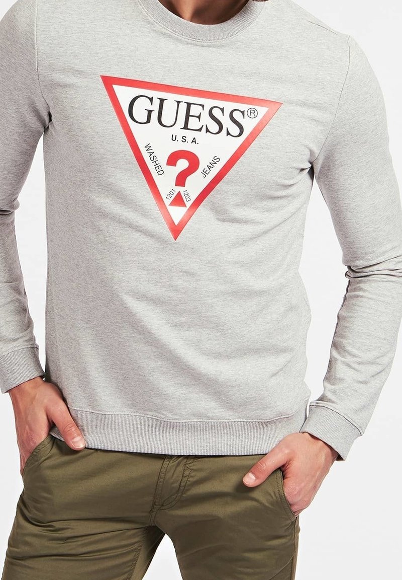 Szara bluza z tkaniny bawełnianej, z dużym czerwonym trójkątnym logo z napisem "GUESS U.S.A." i znakiem zapytania pośrodku.