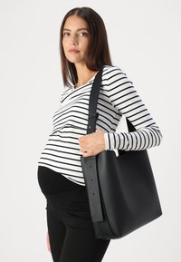 Must värvi nahast käekott, millel on sile tekstuur, laia õlavarre rihmaga ja minimalistlik disain, hoiab inimene, kellel on seljas triibuline topp.
