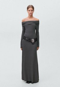 Dlhé šedé šaty s dizajnom bez ramienok, zúženým výstrihom, dlhými rukávmi a širokým čiernym opaskom so zaoblenými akcentmi a kovovým diskom.