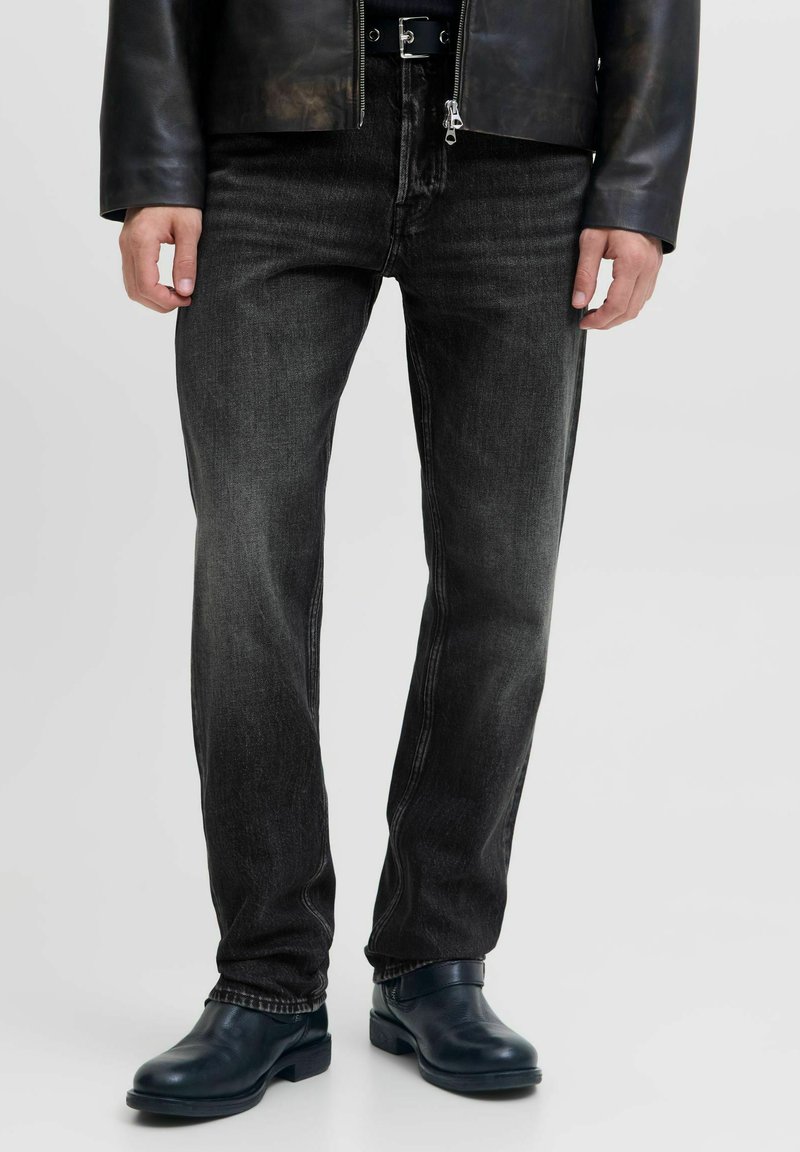 Jeans de mezclilla negra con corte recto, con un ligero desgastado, cierre de cremallera y un diseño clásico de cinco bolsillos. Llevados con botas oscuras.