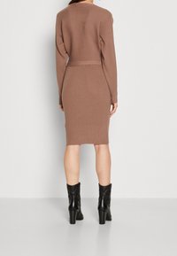 Abito a maglia marrone a coste con maniche lunghe, orlo al ginocchio e design aderente. Abbinato a stivaletti neri con tacco.