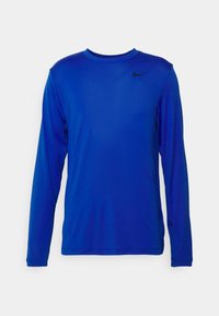 Långärmad, lysande blå träningsskjorta med rund hals och liten svart Nike-swoosh på vänster bröst mot vit bakgrund.