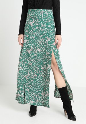 Green floral maxi skirt with thigh-high slit worn with black long-sleeve top and black heeled sock boots.