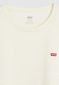 Witte crew-neck t-shirt met horizontale structuur, rode Levi's logo patch op de linkerkant van de borst, en verzorgingslabel in de kraag.