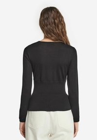 Svart långärmad topp i mjukt tyg, med figursydd midja, rund halsringning och sömlös bakkonstruktion. Matchas med vita byxor.