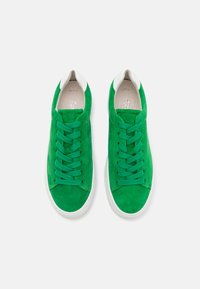 Green suede sneakers with white accents, featuring lace-up design, rounded toe, and textured surface. Flat rubber sole.