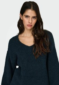 Granatowy dzianinowy sweter z głębokim dekoltem w serek i długimi rękawami, o fakturowanym wykończeniu i luźnym kroju.