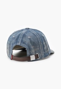 Denimjusterbar caps med en lys blå farge, buet skjerm og brun lærreim med metallspenne, med en falmet tekstur.