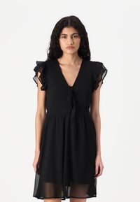 Black dress featuring a V-neck, tie detail at the waist, and ruffled short sleeves. Made of lightweight fabric with a flowy skirt.