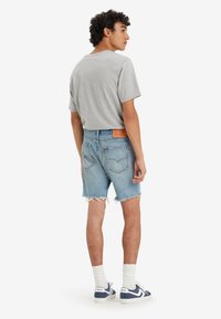 Camiseta de algodón gris combinada con pantalones cortos de denim de color azul claro con dobladillos deshilachados. Calcetines blancos y zapatillas de deporte azul marino completan el conjunto.