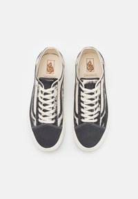Black and cream low-top sneakers with a textured upper, contrasting dark toe cap, and flat laces. Features iconic brand logo on insole.
