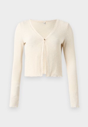 Ribbed, cream-colored cropped cardigan with a V-neck, long sleeves, and a front tie closure. Soft texture with a slightly frayed hem.