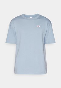 Světle modré tričko s krátkým rukávem vyrobené z bavlny, s malým vyšitým logem na hrudi a kulatým výstřihem. Hladká textura.