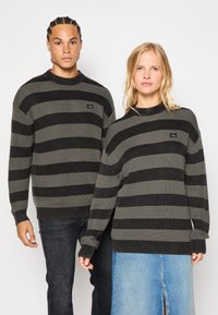 Swetry dziane w paski w kolorze czarnym i szarym, z fakturą ribbed, okrągłym dekoltem, naszywką z logo z przodu oraz długimi rękawami.