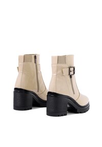 Stivali alla caviglia beige in pelle con texture liscia, dotati di una cerniera laterale, dettaglio con fibbia e tacco spesso nero.