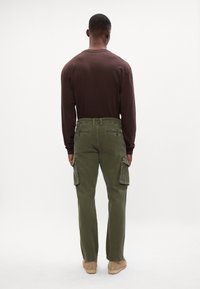 Cargo bukser i olivengrøn med lomme-patches, parret med en brun langærmet skjorte. Minimalistisk design og glat stofstruktur.