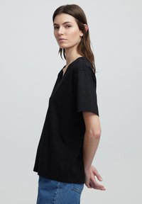 T-shirt nera a maniche corte con scollo a V in cotone, indossata con jeans in denim blu, caratterizzata da una vestibilità comoda e un orlo dritto nella parte inferiore.