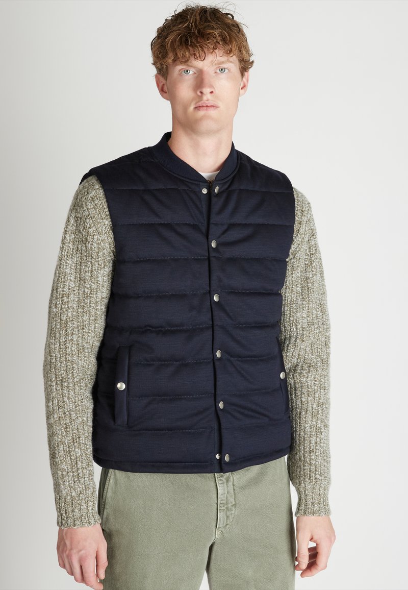 Marineblauer Puffer-Weste mit einem gesteppten Design und silbernen Druckknöpfen, kombiniert mit hellgrauen, strukturierten Strickärmeln. Schmale Passform.