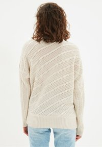 Pull beige clair en tricot avec un motif ondulé, poignets et ourlet côtelés. Coupe décontractée avec une silhouette ample, en tissu texturé.