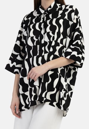 Camicia bianca e nera con un motivo ondulato, maniche corte, colletto e patta dei bottoni. Realizzata in un tessuto leggero e liscio.