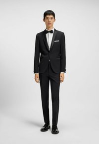 Schwarzer Smoking mit satinierter Revers, weißem Hemd und Fliege. Schlanke Passform, maßgeschneiderte Hose, kombiniert mit glänzenden schwarzen Dressschuhen.