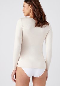 Top fitted a maniche lunghe in beige chiaro, realizzato in un tessuto morbido e liscio. Presenta un collo rotondo e dettagli senza cuciture sulle spalle.
