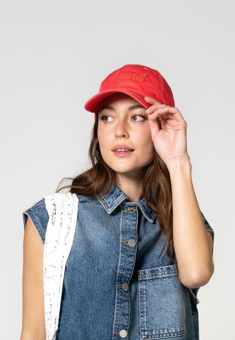 Sarkans kokvilnas beisbola cepure ar izšūtu tekstu, ar izliekta viziera un regulējamu jostu. Apvienota ar džinsu bezpiedurkņu jaku.