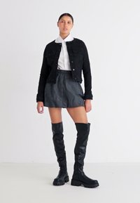 Μαύρο τζάκετ από τζιν, λευκή μπλούζα με γιακά, ριγέ μαύρη φούστα και μπότες μέχρι το γόνατο, με κομψό σχέδιο και υλικά με υφή.