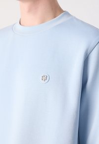 Sweatshirt bleu clair à col rond, fabriqué à partir d'un matériau doux, avec un petit logo brodé sur la poitrine.